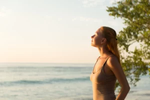 Mulher está numa praia sob o sol da manhã, Ela se expõe ao sol devido a carência de vitamina D.