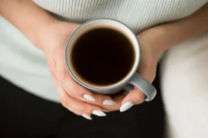 Mãos femininas seguram uma xícara com café, uma das bebidas que contém cafeína.