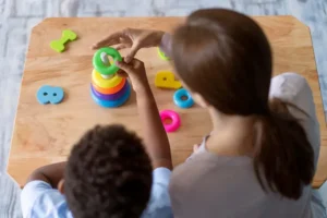 Criança está em uma uma mesa brincando ao lado de psicóloga. Ela apresenta sinais de autismo.