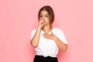 Mulher coloca uma mão abaixo do pescoço e outra leva à boca porque tem soluço.