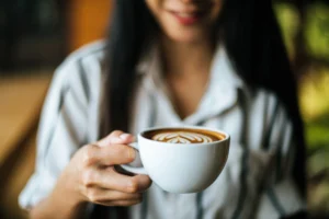 Mulher tomando café durante o trabalho, representando o impacto do excesso na produtividade.